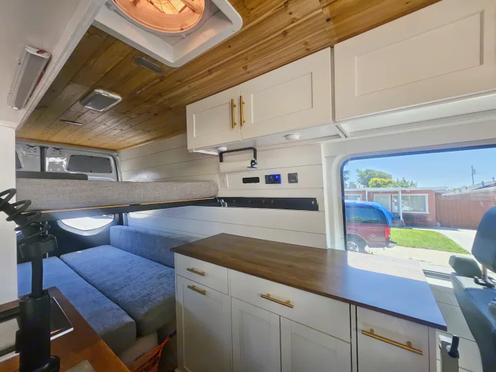 Spacious and modern RV rental interior with a wooden ceiling, white cabinets, and cozy sleeping/seating areas.. Mercedes Benz Sprinter 2020