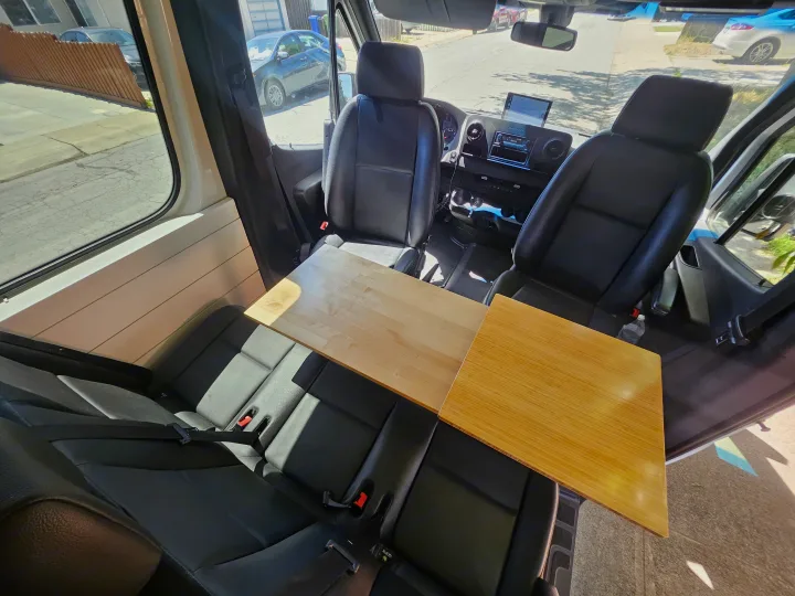 RV rental interior with front and rear seating, plus a versatile wooden table, ideal for dining or work.. Mercedes Benz Sprinter 2020