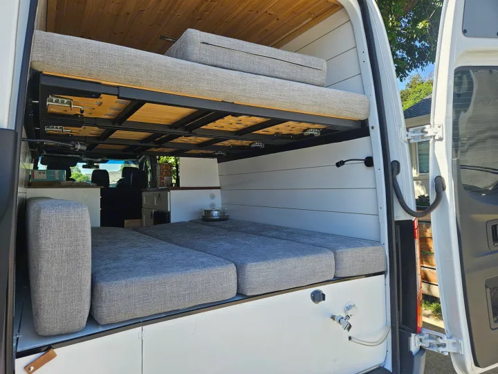 Spacious rv rental interior featuring a bunk bed setup, comfortable gray cushions, and white paneling, ideal for mobile living.. Mercedes Benz Sprinter 2020