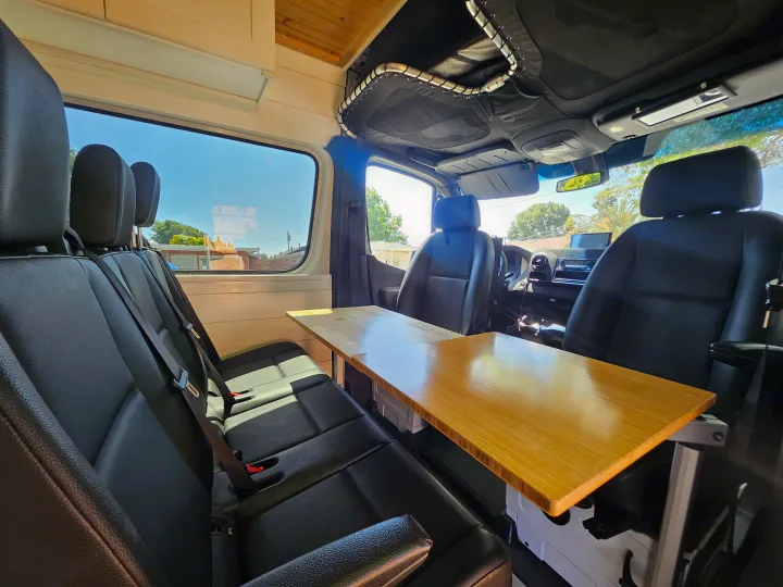 Spacious RV rental interior with comfy seating and a wooden table, perfect for travel & mobile work.. Mercedes Benz Sprinter 2020