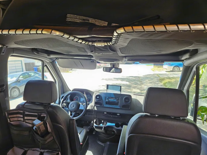 Inside a Mercedes Sprinter RV rental. Front cabin view with steering wheel, dashboard, and custom mesh overhead storage.. Mercedes Benz Sprinter 2020