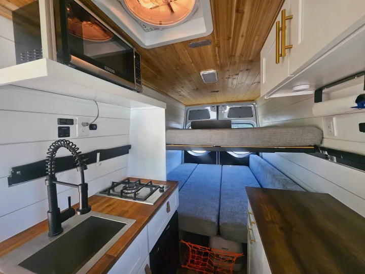 Cozy camper van rv rental interior: kitchen with microwave, sink, stove, and a versatile bunk bed sleeping area.. Mercedes Benz Sprinter 2020