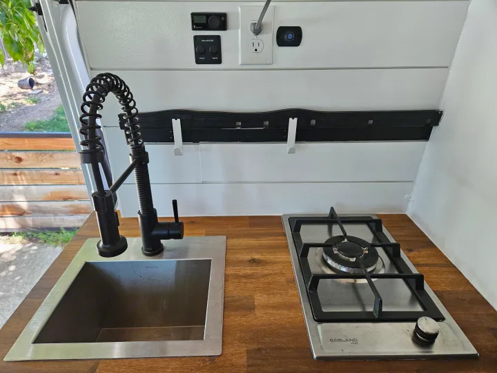 RV rental: well-equipped kitchenette features a modern sink, pull-down faucet, gas stove, and controls for tank heaters. Compact & functional.. Mercedes Benz Sprinter 2020