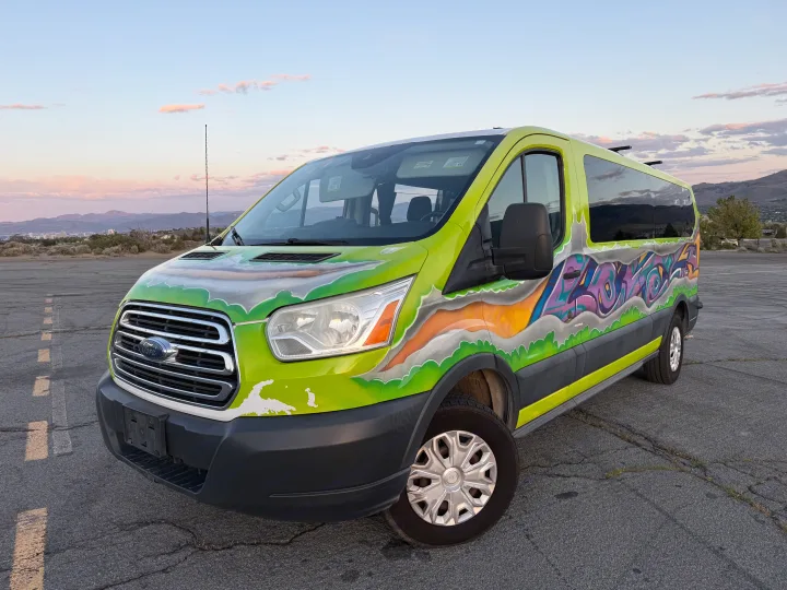 Vibrant custom-painted Ford Transit van with graffiti art, possibly an rv rental, parked outdoors with mountains and city in the background.. Ford Transit 2017