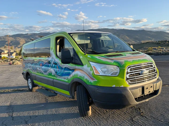 Bright green Ford Transit RV rental, custom-painted with graffiti art, parked outdoors with mountains & blue sky.. Ford Transit 2017