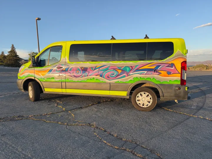 Vibrant lime-green graffiti RV rental van, ready for adventure, parked on cracked asphalt under a clear blue sky.. Ford Transit 2017