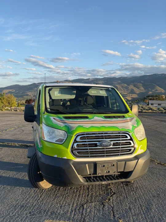 Front view of a bright green Ford Transit RV rental van, parked outdoors with mountains and a blue, cloudy sky.. Ford Transit 2017
