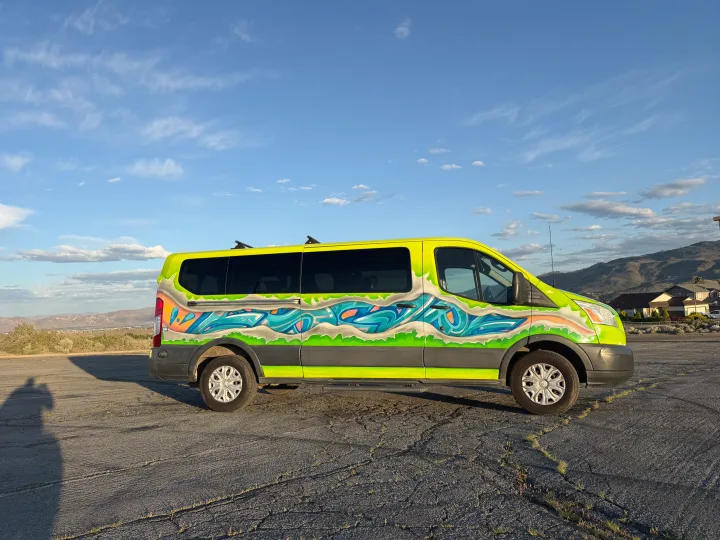 A bright yellow RV rental van, customized with graffiti artwork, is parked on cracked pavement with mountains in the background.. Ford Transit 2017