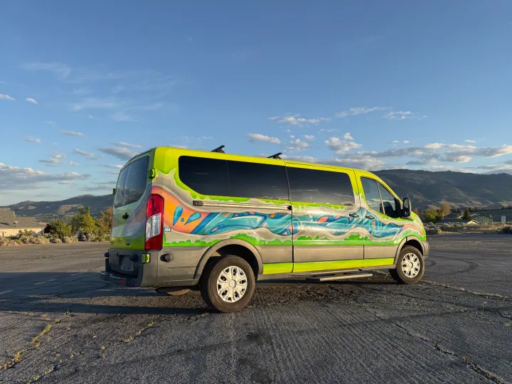 Adventure-ready RV rental van: vibrant custom paint, neon green with a blue/orange mural, parked outdoors with mountains as a backdrop.. Ford Transit 2017