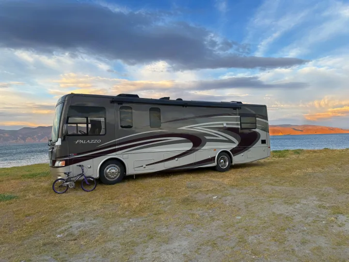 Thor Palazzo rv rental by a serene lake, mountains, and a child's bike. Ready for your next adventure!. Thor Palazzo 2014