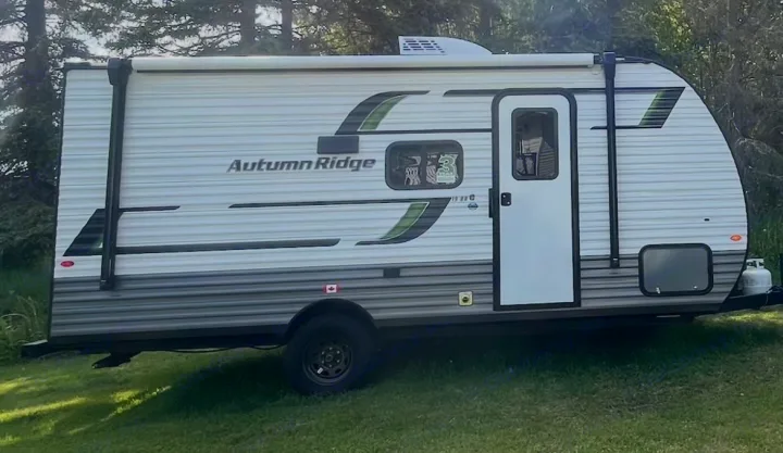 Side view of an Autumn Ridge travel trailer, an excellent RV rental option, parked on grass. Features a door, windows, and awning.. Starcraft Autumn Ridge 2025