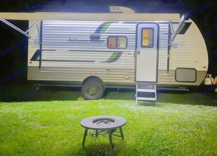 Night camping with this cozy rv rental: illuminated travel trailer, extended awning, and a fire pit on grass.. Starcraft Autumn Ridge 2025