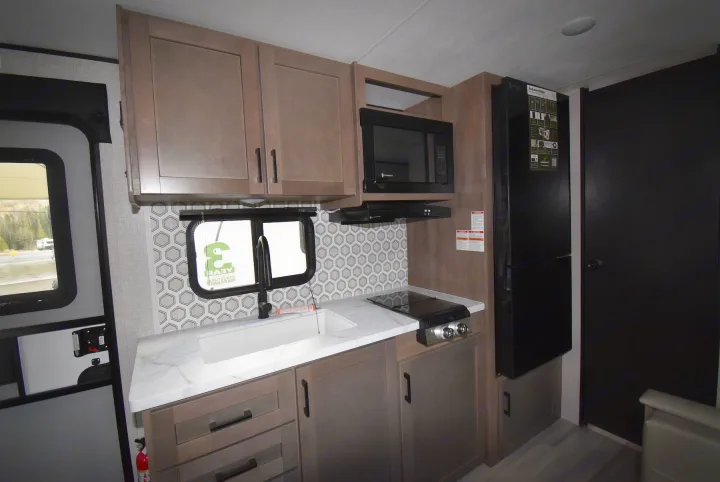 Modern RV rental kitchen with light wood cabinets, sink, stovetop, microwave, and refrigerator. Perfect for comfortable camping.. Starcraft Autumn Ridge 2025