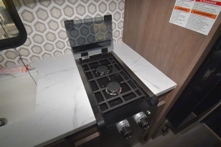 RV rental's compact kitchen setup includes a two-burner gas stove, sink, and patterned backsplash on a white counter.. Starcraft Autumn Ridge 2025