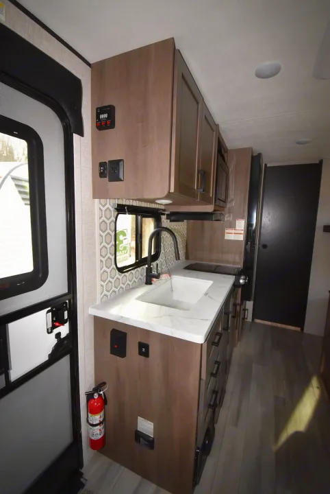 Explore this RV rental's modern galley with a sink, cooktop, microwave, fridge, and stylish wood cabinets.. Starcraft Autumn Ridge 2025