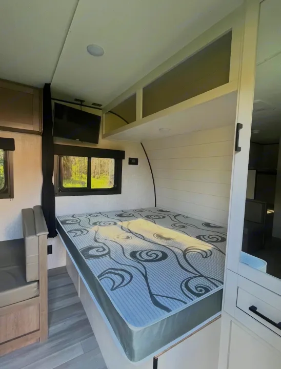 Bright RV rental interior showing a bed with patterned mattress, dinette, TV, and windows with scenic views.. Starcraft Autumn Ridge 2025