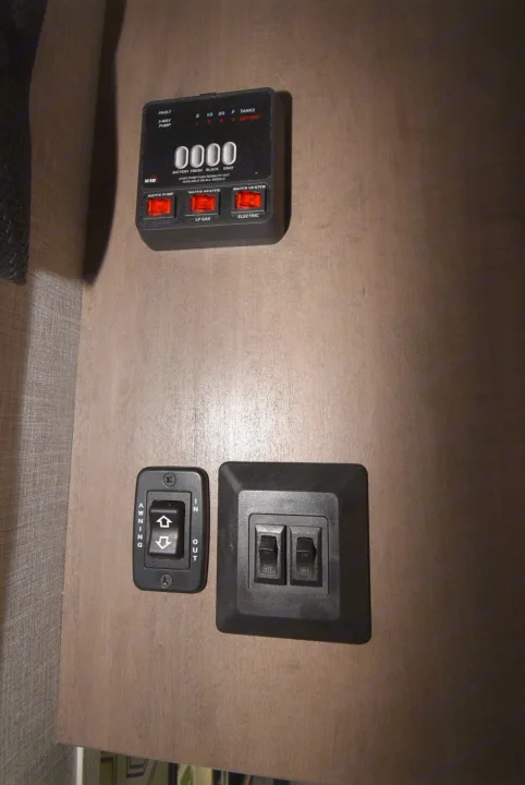 RV rental control panel: KIB monitor displays tank/battery levels, water heater settings. Awning and other switches on wooden wall.. Starcraft Autumn Ridge 2025