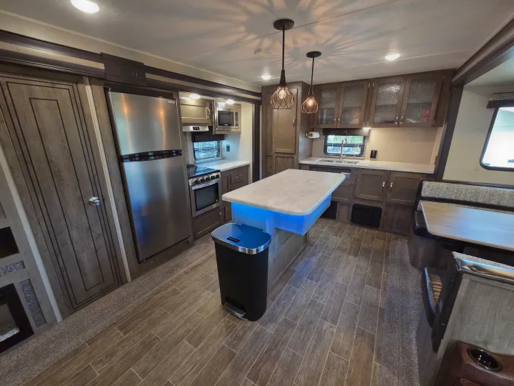 Spacious RV rental kitchen interior featuring stainless appliances, island with cool blue lighting, wood-look flooring, and dining booth.. Forest River Palomino Puma 2020