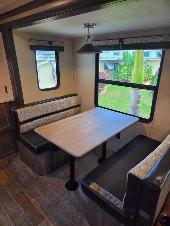 RV rental dinette area with patterned benches, light-colored table, and large windows offering an outdoor view.. Forest River Palomino Puma 2020