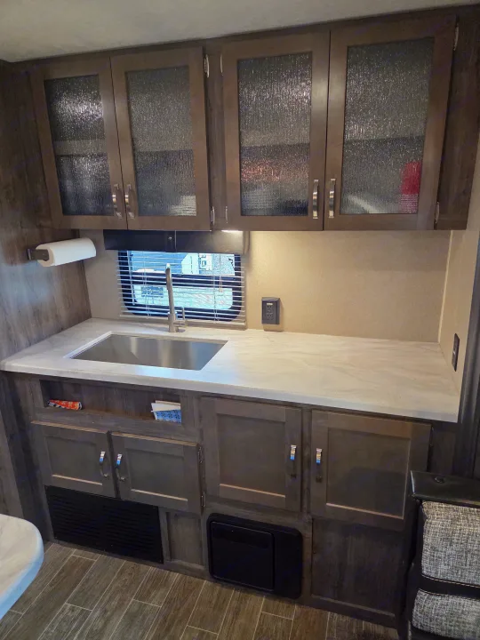 Modern RV rental kitchen with frosted glass cabinets, stainless steel sink, ample countertop, and utility features.. Forest River Palomino Puma 2020