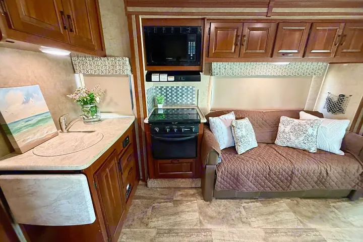Cozy RV rental interior with a well-equipped kitchen featuring a stove, microwave, and sink, plus a comfortable sofa.. Forest River Sunseeker 2016