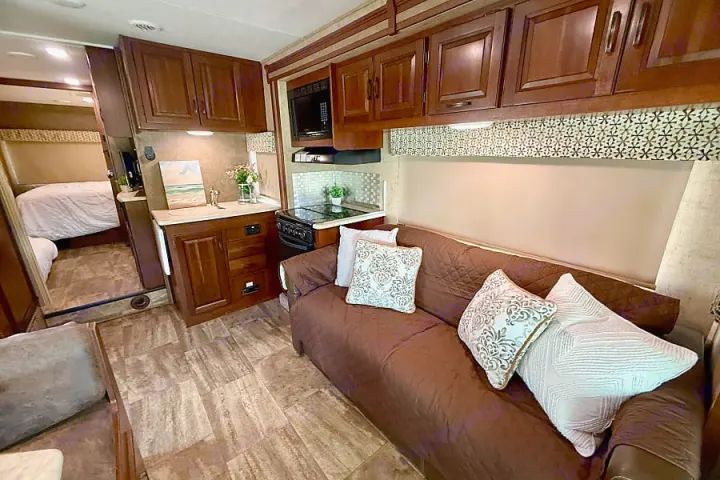 Spacious RV rental interior: kitchen with microwave/stove, living area with sofa, and cozy bedroom. Ideal for road trips.. Forest River Sunseeker 2016