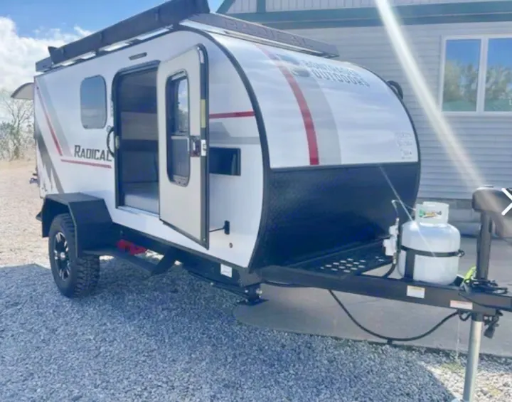 White "Radical" teardrop RV rental, a compact travel trailer with an open door, awning, and propane tank. Ready for adventure!. Bontrager Outdoors 12RAD 2025