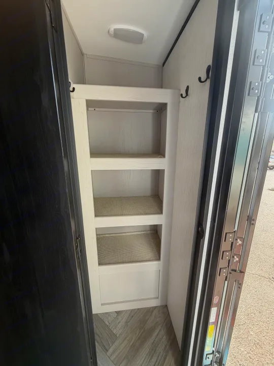 Inside an RV rental's well-organized storage closet, featuring three shelves with liners, wall hooks, and a ceiling light.. Heartland RVs Mallard 2023