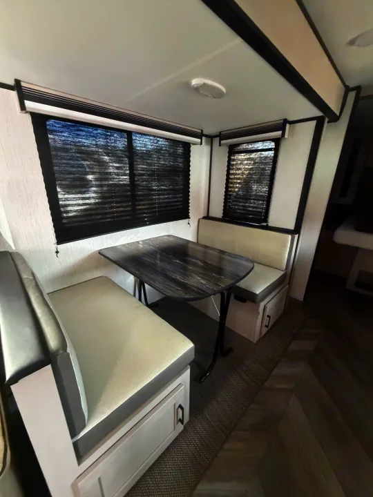 Cozy RV rental dinette with gray and white benches, a dark marbled table, and black window blinds.. Heartland RVs Mallard 2023