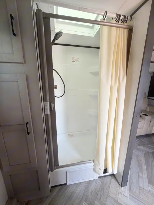 This image captures a clean RV rental shower with a bright skylight, handheld showerhead, and curtain, ready for comfortable travel.. Heartland RVs Mallard 2023