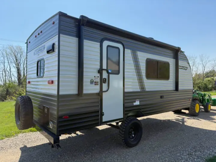 This rugged off-road travel trailer, perfect for an rv rental, features heavy-duty tires and a rear spare, parked on gravel.. Sunset Park RV Sun Lite LTD 2025