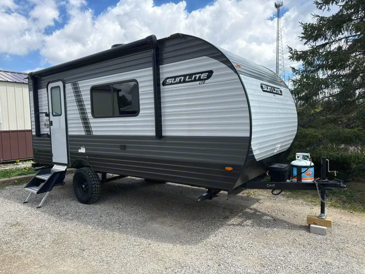 This modern Sun Lite LTD RV rental features an all-terrain tire & propane tank, parked on gravel, ready for adventure.. Sunset Park RV Sun Lite LTD 2025