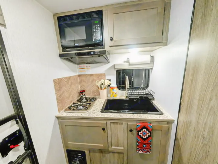 This compact RV rental kitchen features a microwave, stove, sink, and ample storage, perfect for your travels.. Sunset Park RV Sun Lite LTD 2025