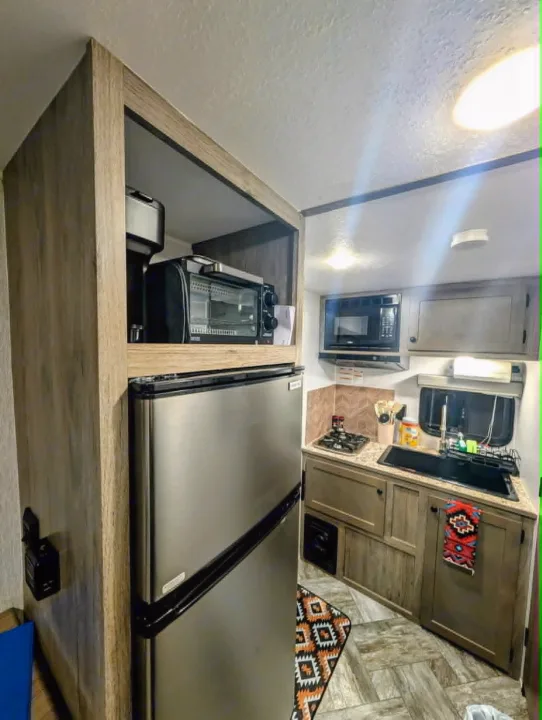 Compact kitchen in an RV rental, featuring a fridge, microwave, stove, sink, and coffee station. Great for travel meals.. Sunset Park RV Sun Lite LTD 2025
