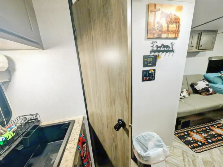 RV rental interior featuring a kitchen sink, wooden door, control panels, cozy sofa, and a colorful floor rug.. Sunset Park RV Sun Lite LTD 2025