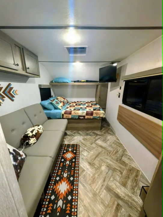 Cozy RV rental interior featuring a sofa, bed, bunk, TV, and Southwestern-inspired decor on herringbone flooring.. Sunset Park RV Sun Lite LTD 2025