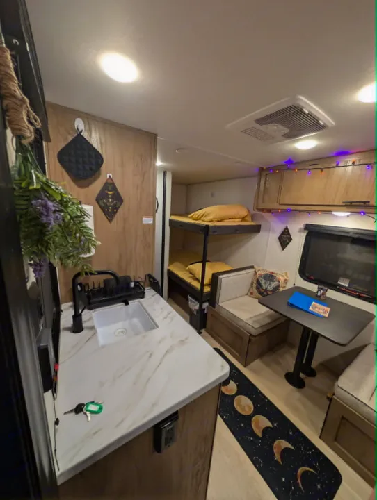 RV rental interior: kitchenette, bunk beds, and a dinette. Features a moon rug, string lights, and witchy decor for a cozy atmosphere.. Forest River Cherokee Wolf Pup 2025