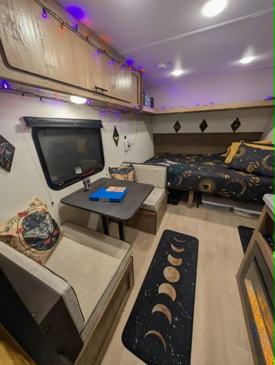 Charming RV rental interior featuring a dinette, comfy bed with moon decor, and string lights for a cozy getaway.. Forest River Cherokee Wolf Pup 2025
