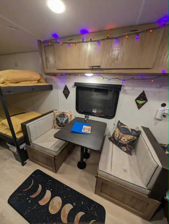Purple and orange string lights illuminate this cozy RV rental interior with bunk beds, dinette, and moon rug.. Forest River Cherokee Wolf Pup 2025