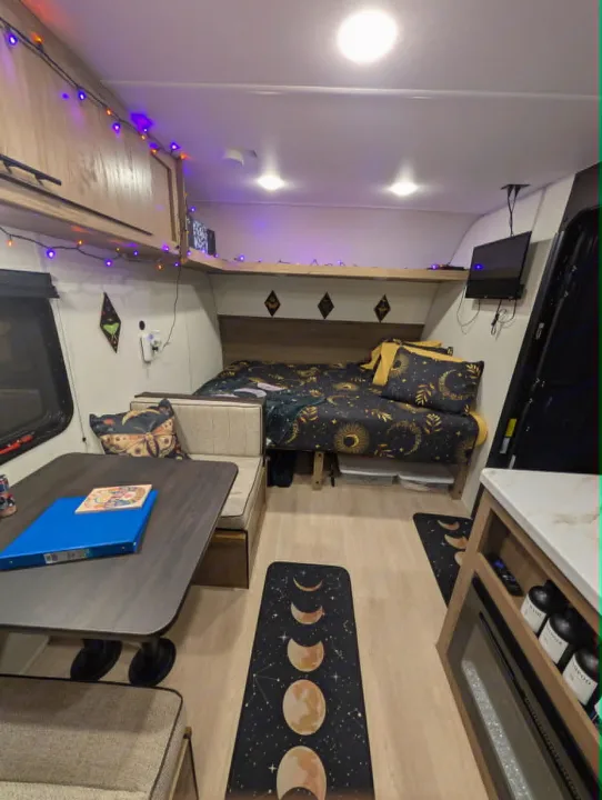 Cozy rv rental interior with celestial-themed bedroom, dining area, and moon phase mats. String lights add warmth.. Forest River Cherokee Wolf Pup 2025