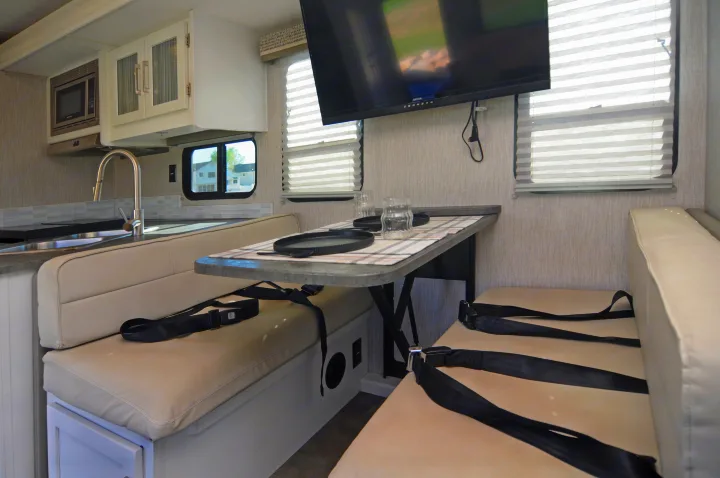 RV rental interior featuring a modern kitchen with microwave, sink, and a cozy dinette with TV and seatbelts.. Coachmen Pursuit 2022