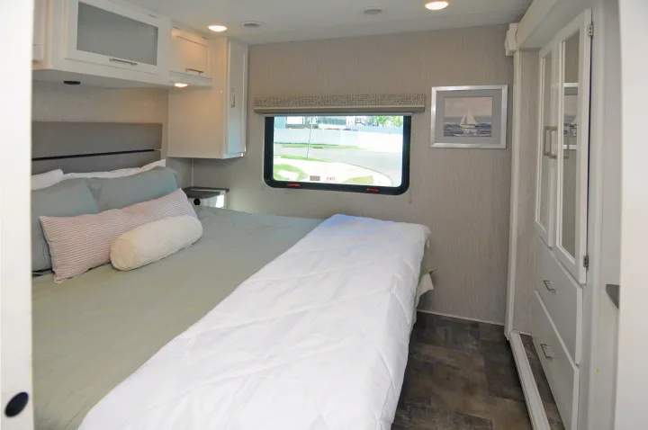 This comfortable RV rental bedroom features a neutral bed, overhead storage, a window, and a wardrobe with drawers.. Coachmen Pursuit 2022