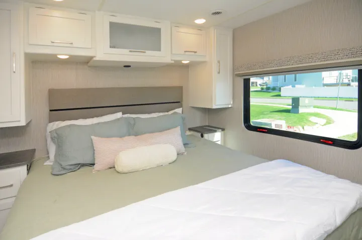Modern RV rental bedroom with a comfy bed, white cabinets, and a window offering a suburban view for your travels.. Coachmen Pursuit 2022