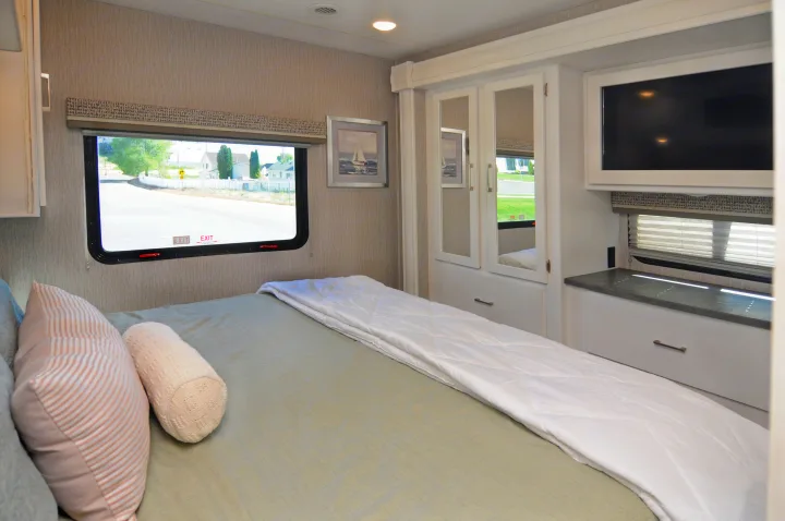 This RV rental bedroom features a comfy bed, window with a view, mirrored closet, and TV for a relaxing journey.. Coachmen Pursuit 2022