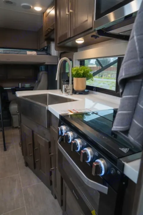 Functional rv rental kitchen: a view of the sink, modern stove, microwave, & cabinetry within a cozy RV interior.. Forest River Coachmen Mirada 2022