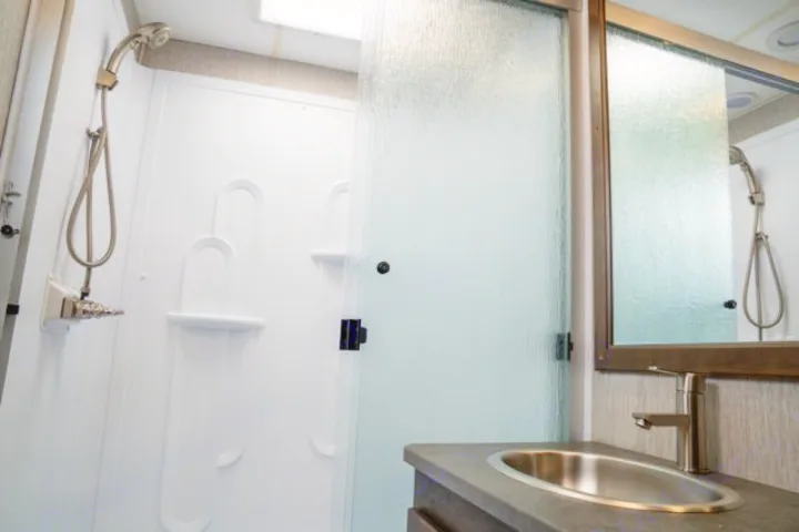 Functional rv rental bathroom with a white shower, frosted glass door, and modern vanity with a stainless steel sink.. Forest River Coachmen Mirada 2022