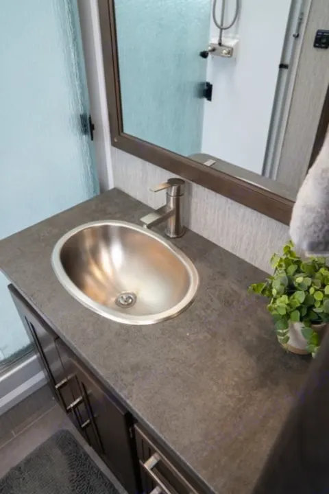 Modern RV rental bathroom with a sleek stainless steel sink, dark countertop, and frosted shower door.. Forest River Coachmen Mirada 2022