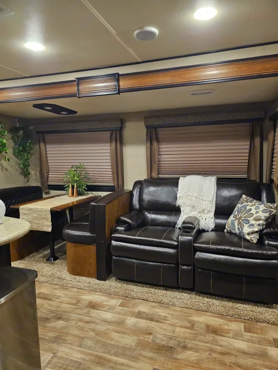 Cozy RV rental interior with dark leather sofa, comfortable dining booth, and stylish wood-look flooring.. Grand Design Reflection 2016