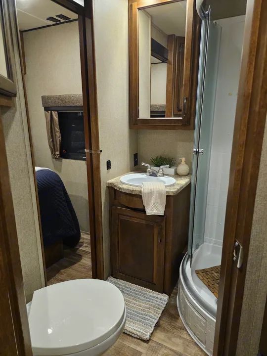 Compact RV rental bathroom featuring a toilet, sink vanity with mirror, and a corner shower. Ideal for travel comfort.. Grand Design Reflection 2016