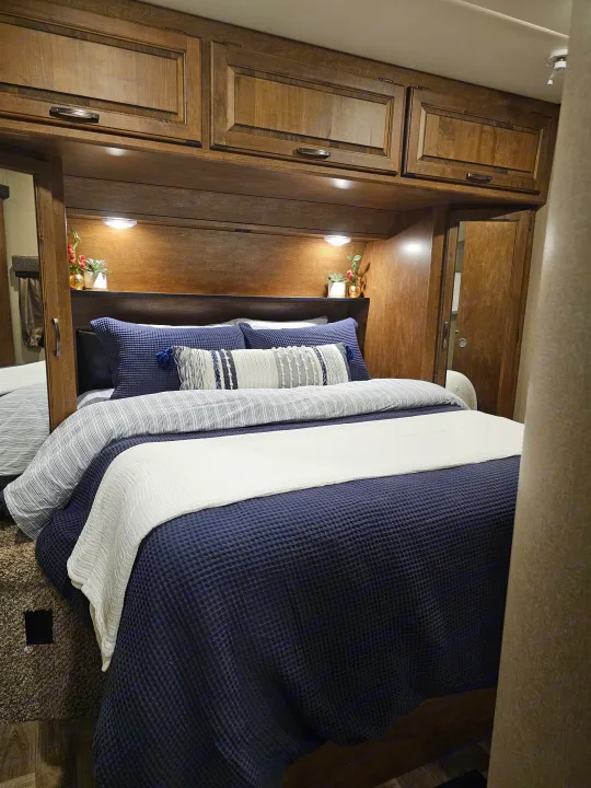 Cozy RV rental bedroom with dark wood cabinets, blue bedding, and soft lighting for a comfortable stay.. Grand Design Reflection 2016